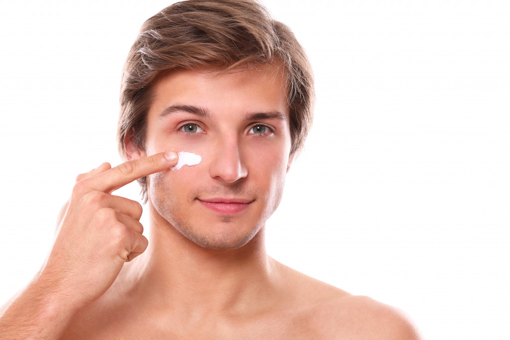 man putting cream on his cheeks