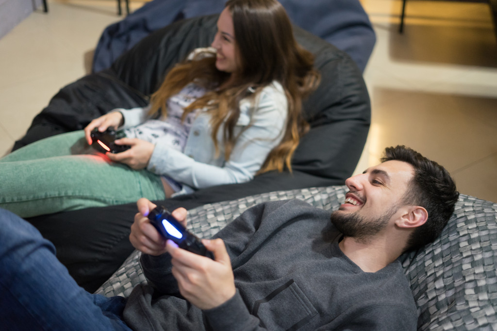 Two gamers playing a console game while lying down on a pair of bean bag chairs