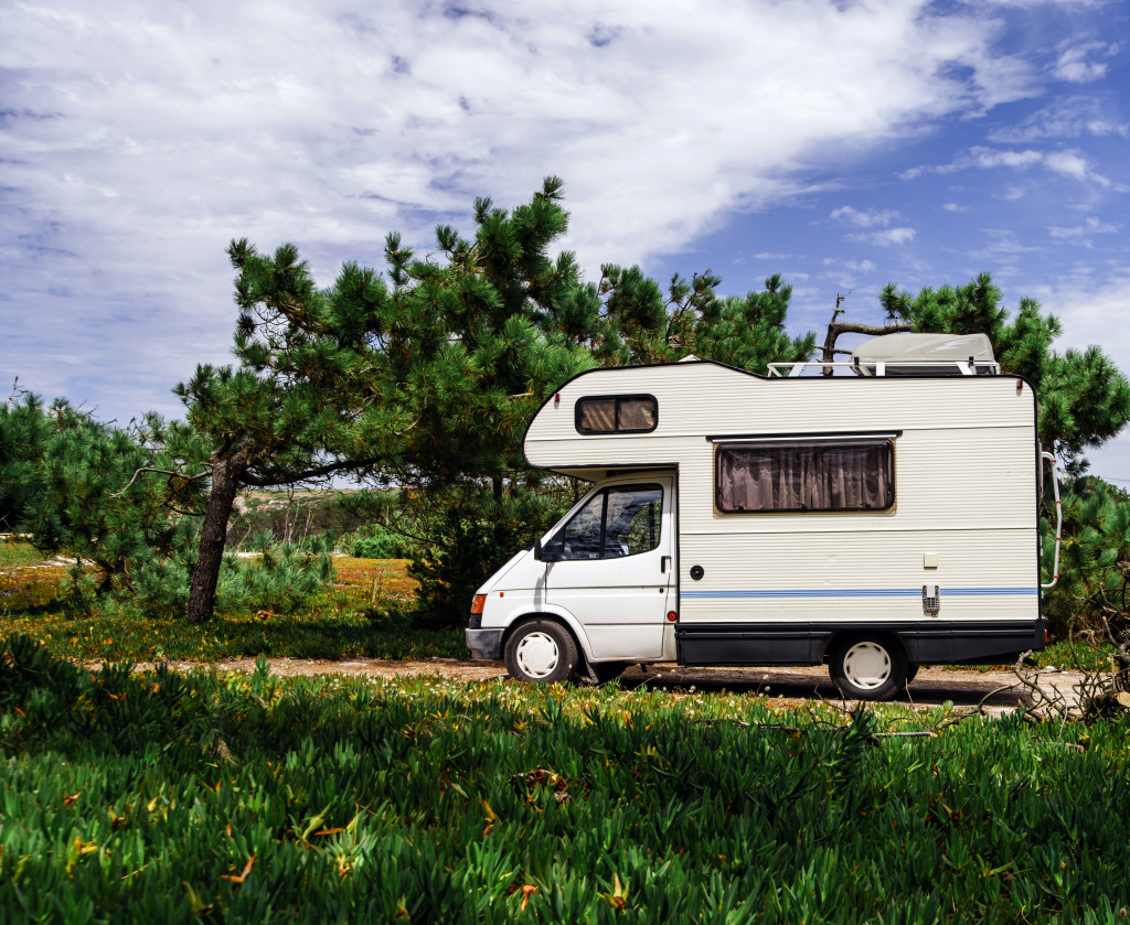 big RV parked in the middle of forested area with grass fields